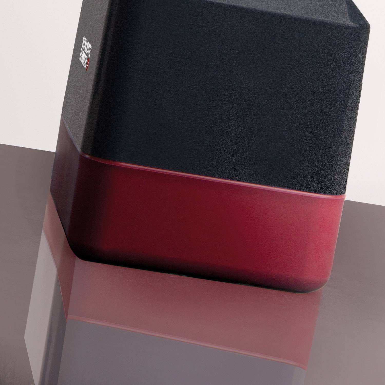 Sześcienny głośnik w dwóch kolorach - czerwonym i czarnym, umieszczony na lustrzanej powierzchni.