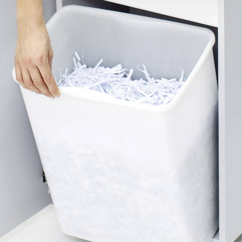 Ręka wrzuca pocięte na drobne kawałki papier do białego kosza na śmieci.