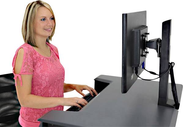 Kobieta pisze na klawiaturze komputera przy czarnym pulpicie stojącym. Ma na sobie różową górę i patrzy na ekran.