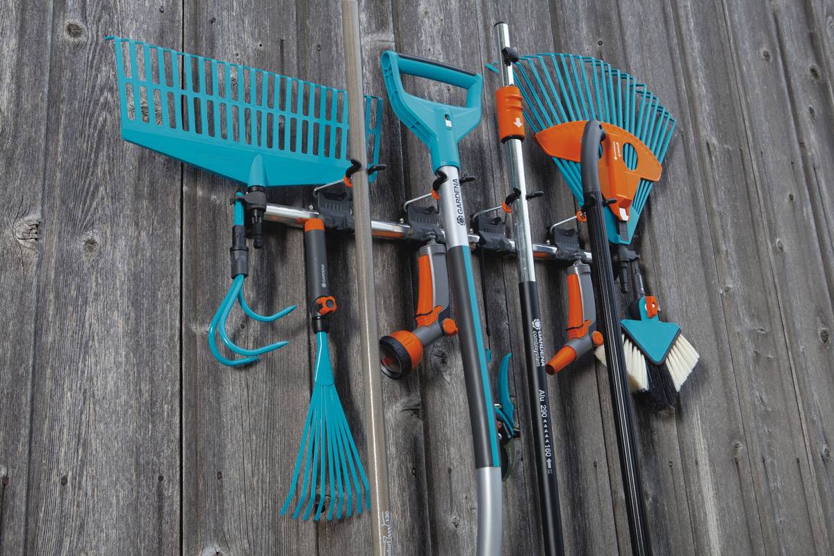 Narzędzia ogrodnicze, w tym grabie i łopata, starannie powieszone na drewnianej ścianie, świadczą o organizacji i efektywnym przechowywaniu.