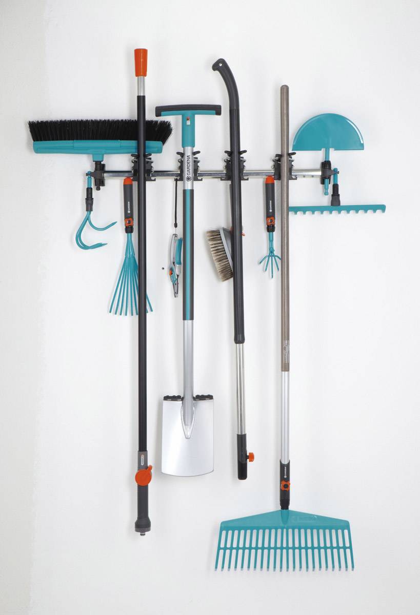 Narzędzia ogrodnicze zorganizowane na wieszaku ściennym: miotła, łopata, grabie, przekładacz i szczotka.