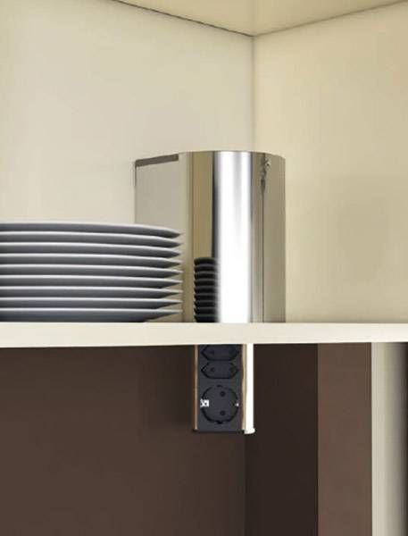 Narożnik regału z srebrnym naczyniem i stosem białych talerzy. Poniżej, po stronie, wbudowane są dwa gniazdka elektryczne.