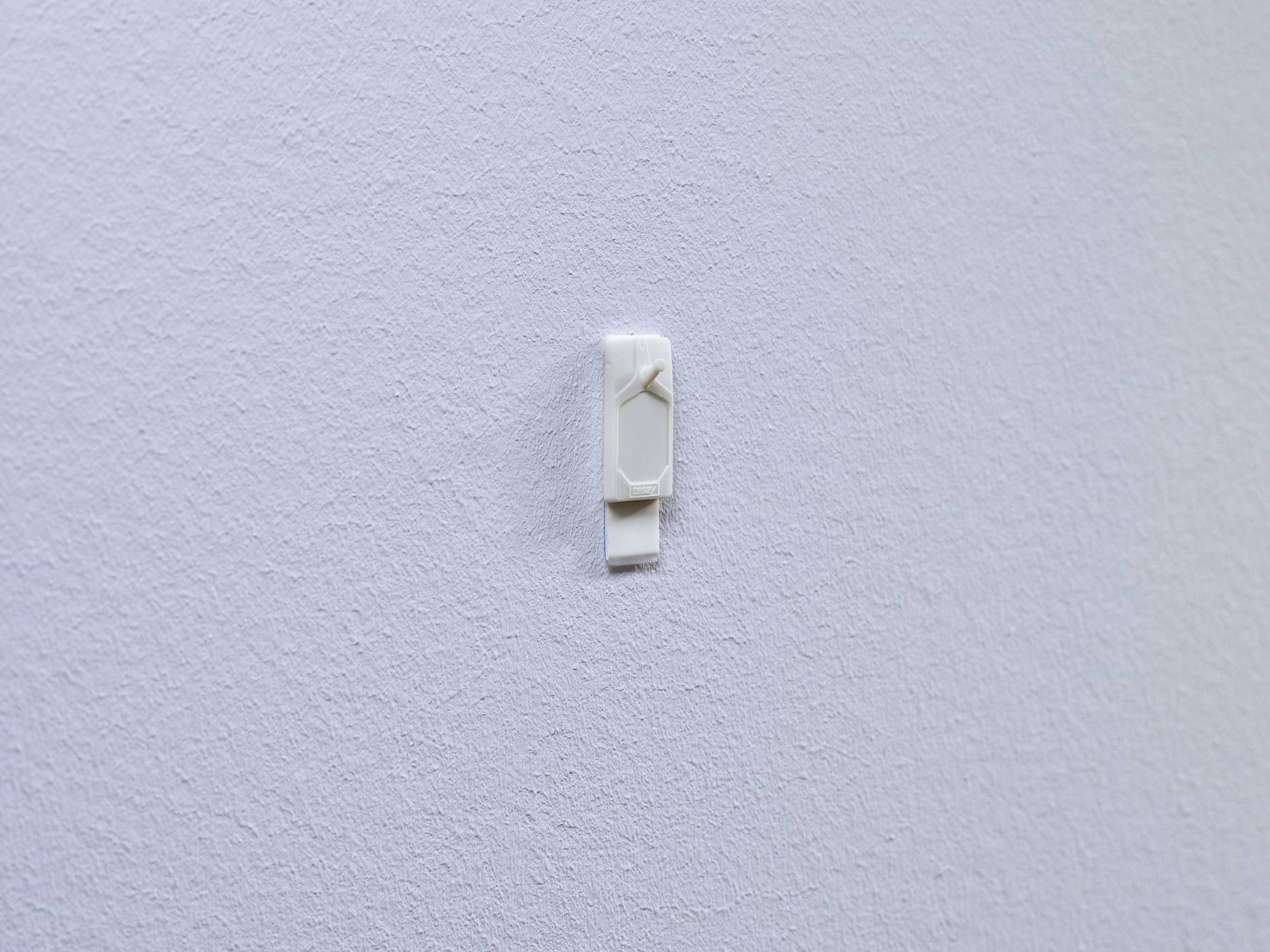 Biały hak zamontowany na strukturalnej białej ścianie, przeznaczony do zawieszania mniejszych przedmiotów.