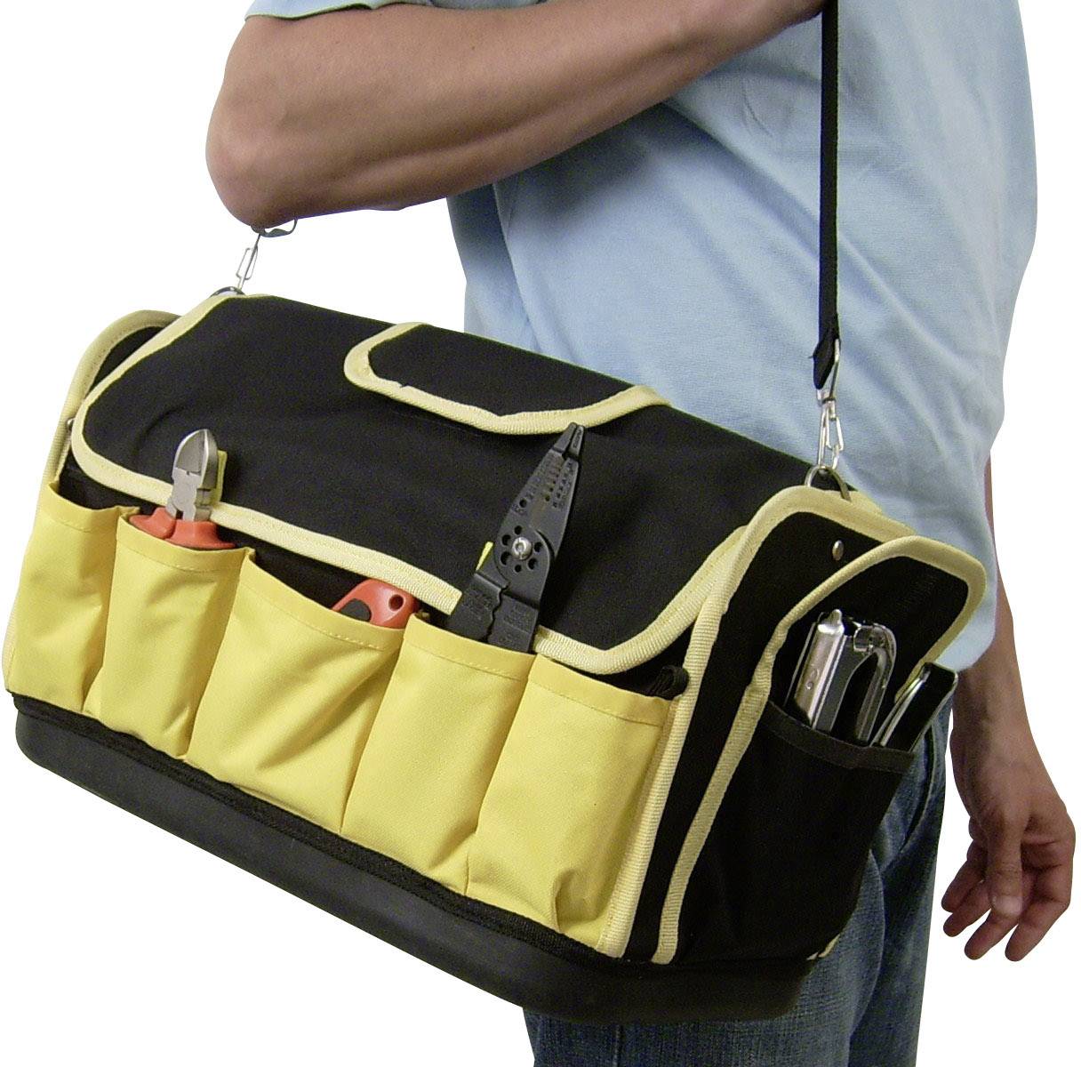 Osoba trzyma dużą, czarno-żółtą torbę narzędziową z wieloma przegródkami i narzędziami, w tym szczypcami i śrubokrętem.