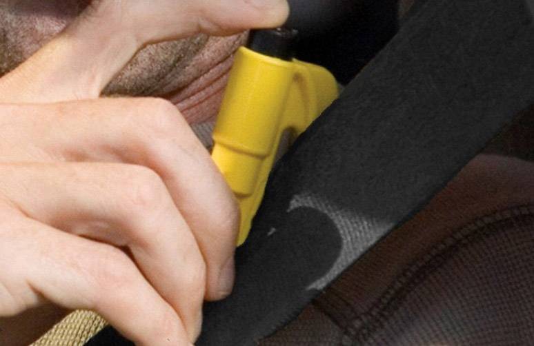 Osoba trzyma żółty nóż do pasów bezpieczeństwa i przecina nim pas bezpieczeństwa w samochodzie.