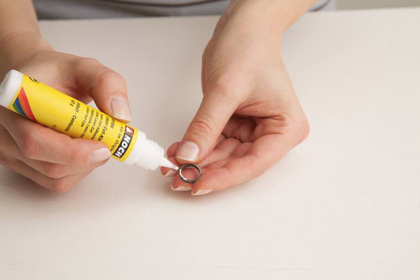 Osoba nanosi klej z żółtej tubki na mały metalowy pierścień.