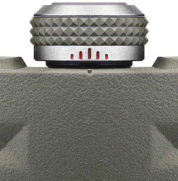 Zbliżenie metalowego pokrętła z czerwonym oznaczeniem na szarym, teksturowanym tle.