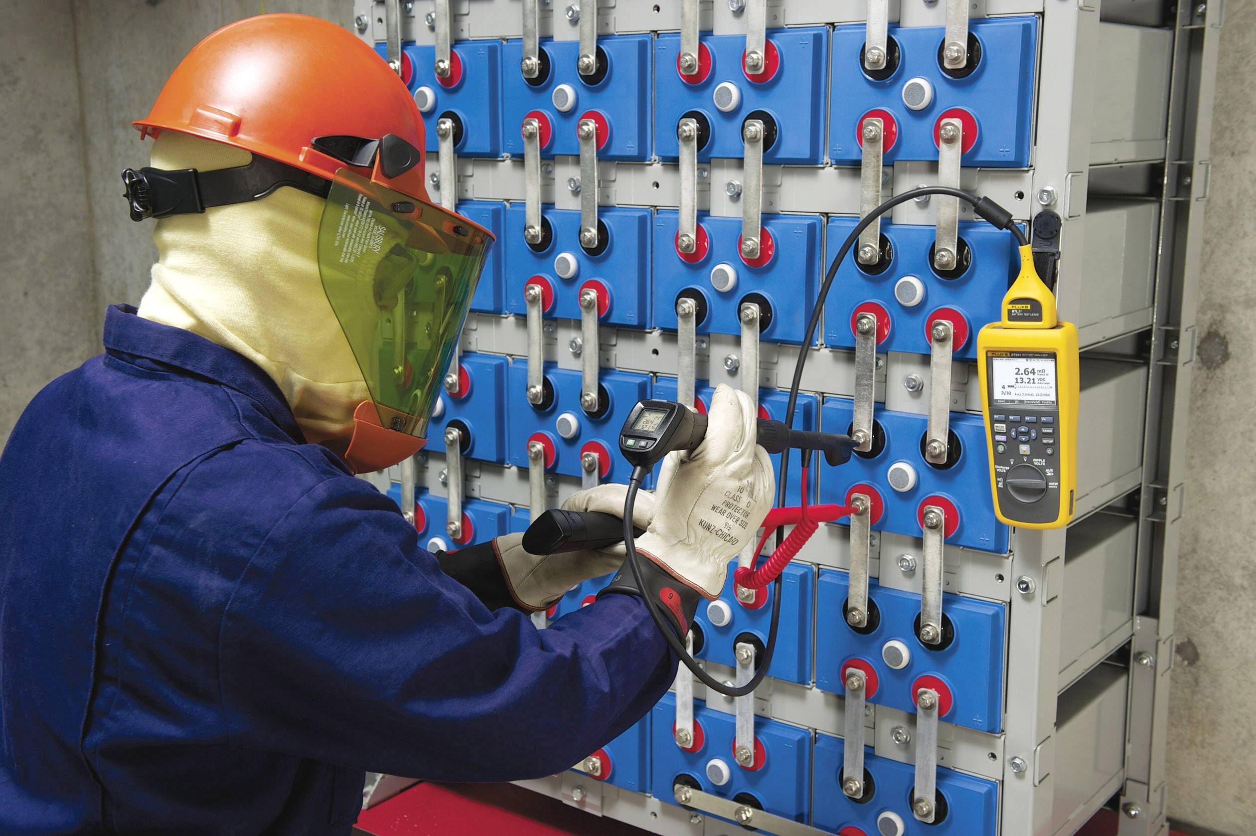 Technik w stroju ochronnym sprawdza napięcie dużej instalacji bateryjnej w środowisku przemysłowym za pomocą miernika.