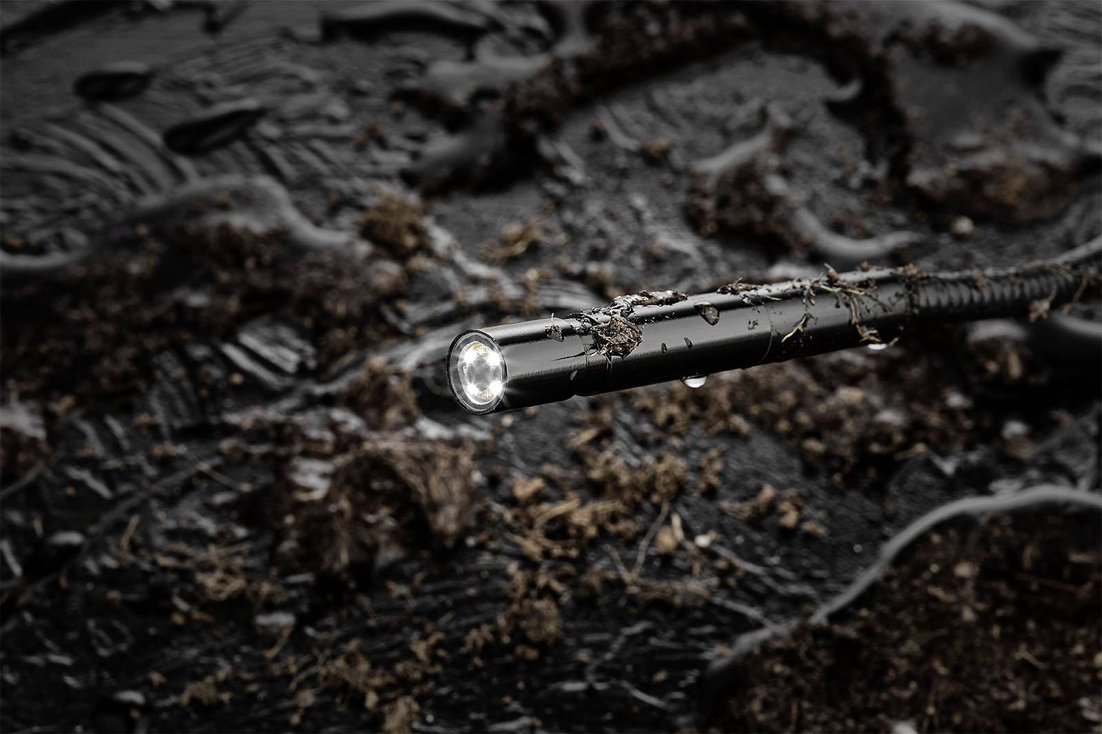 Czarny wąż w zbliżeniu, leżący w gliniastej glebie, z jasnym światłem na końcu.