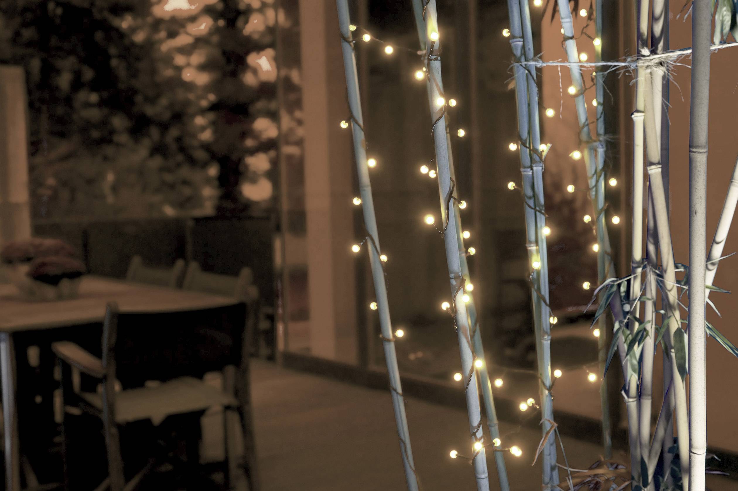 Girlandy świetlne zwisają z bambusowych kijów we wnętrzu, obok stół z krzesłami, które tworzą przytulną atmosferę.