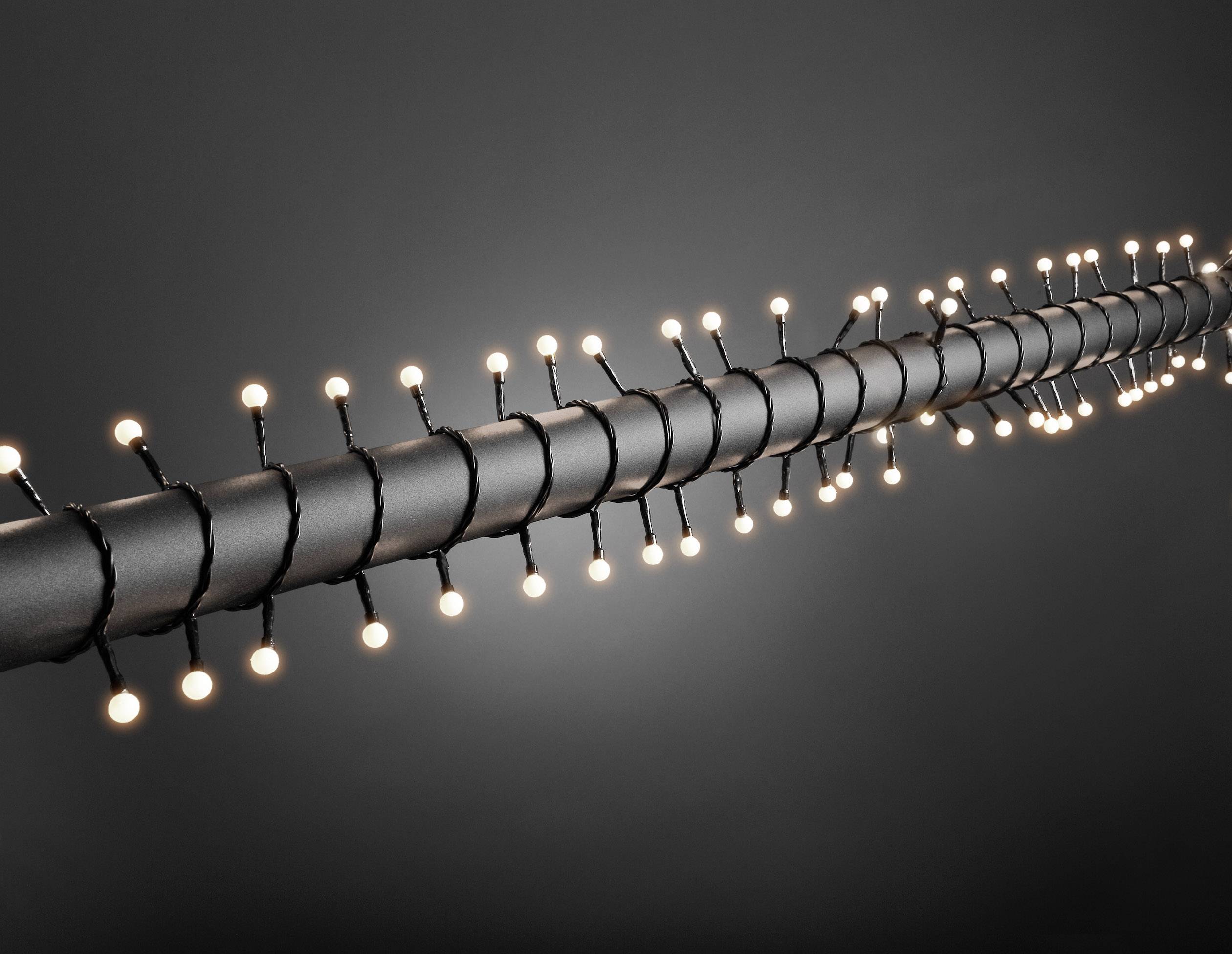 Łańcuch świetlny ułożony spiralnie wokół rury na szarym tle.