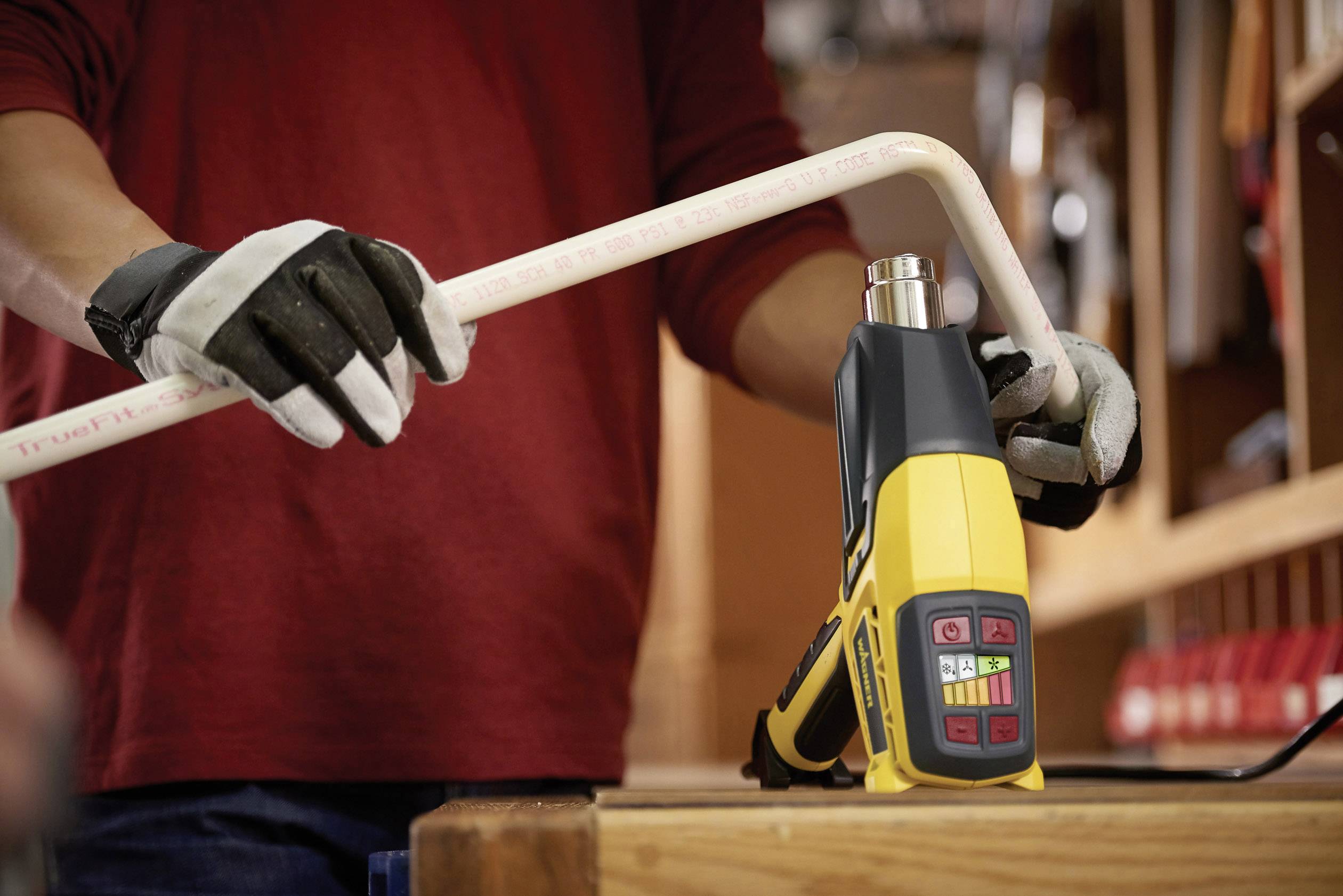 Osoba zgina rurę za pomocą żółtego dmuchawy gorącego powietrza w warsztacie.