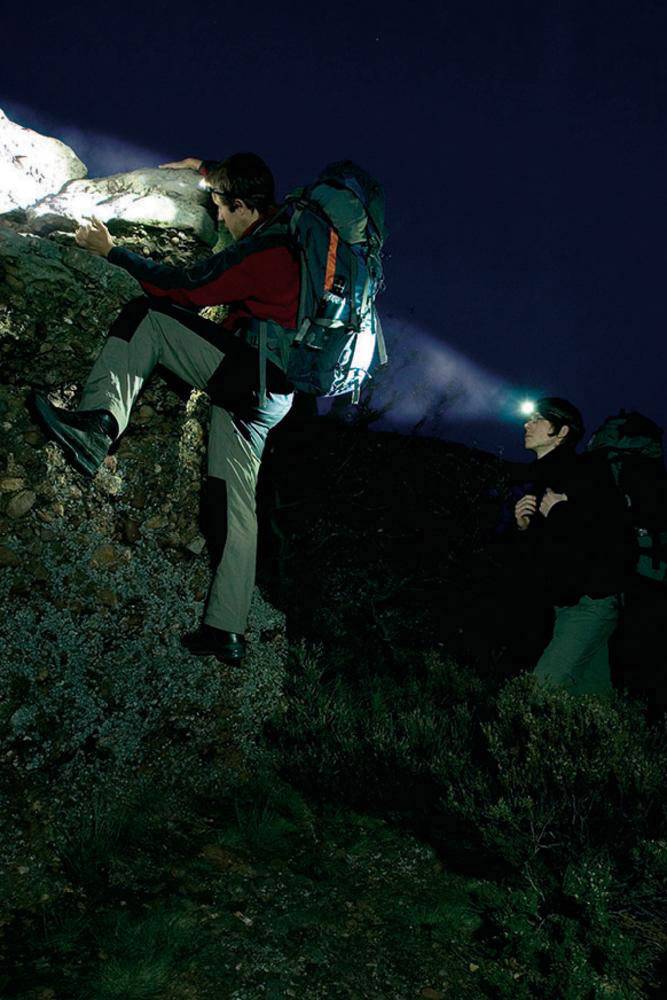 Dwie osoby wspinają się w nocy na skałę przy świetle latarek; jasne światła oświetlają im drogę.