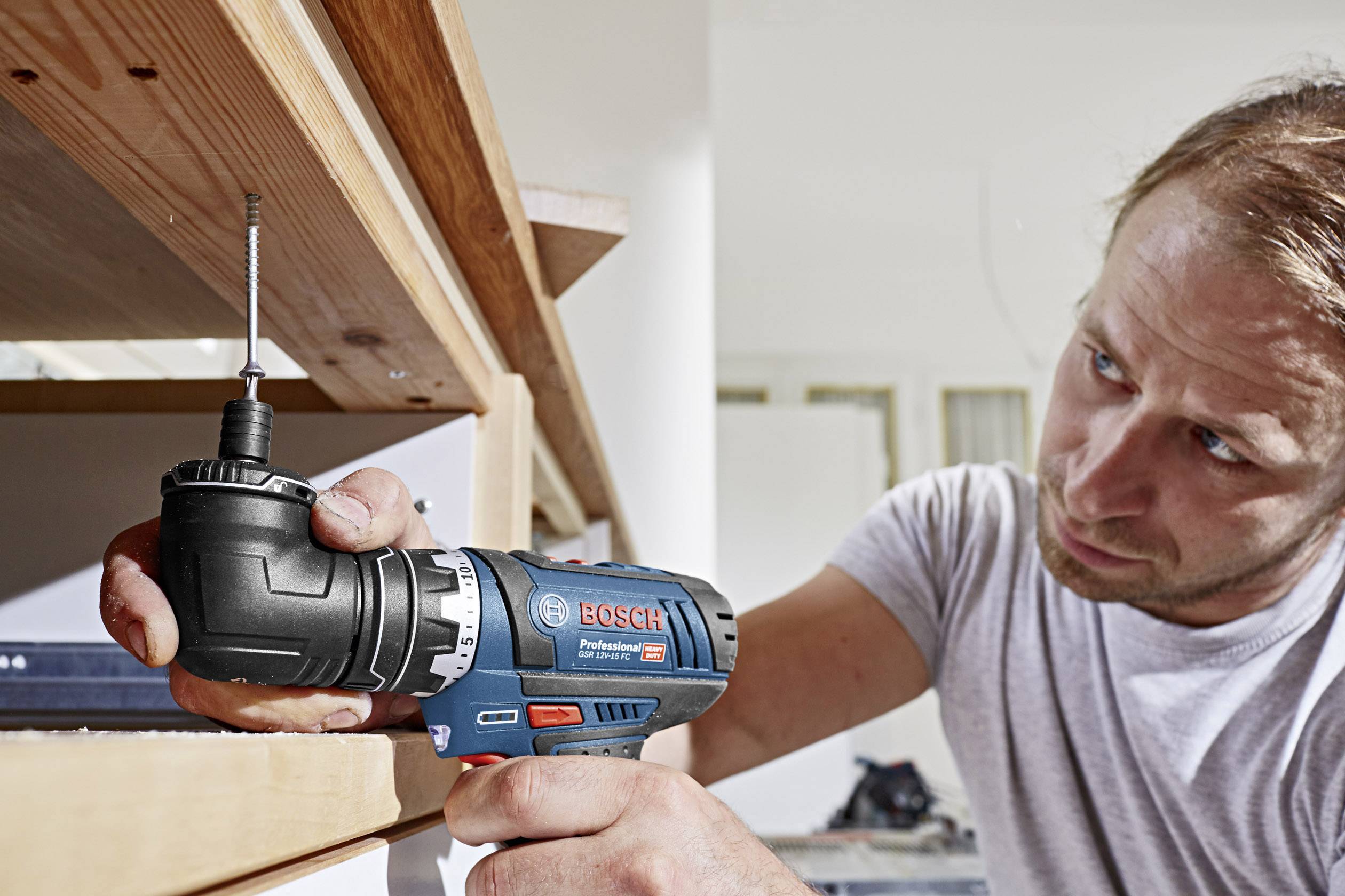 Mężczyzna używa elektrycznego wkrętarko-wiertarki, aby zamocować półkę. Jest całkowicie skupiony na wykonywaniu pracy.