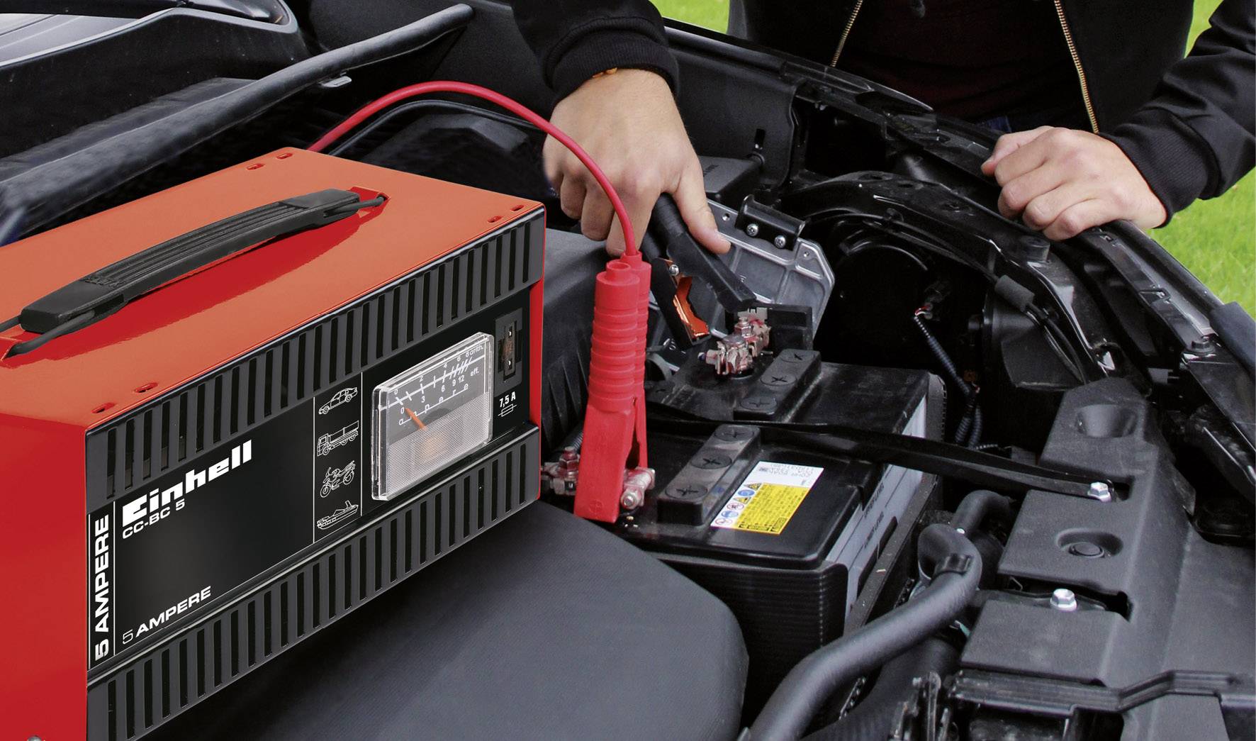 Osoba ładuje akumulator samochodowy za pomocą ładowarki. Ładowarka wskazuje 6 amperów. Kable są podłączone do baterii.