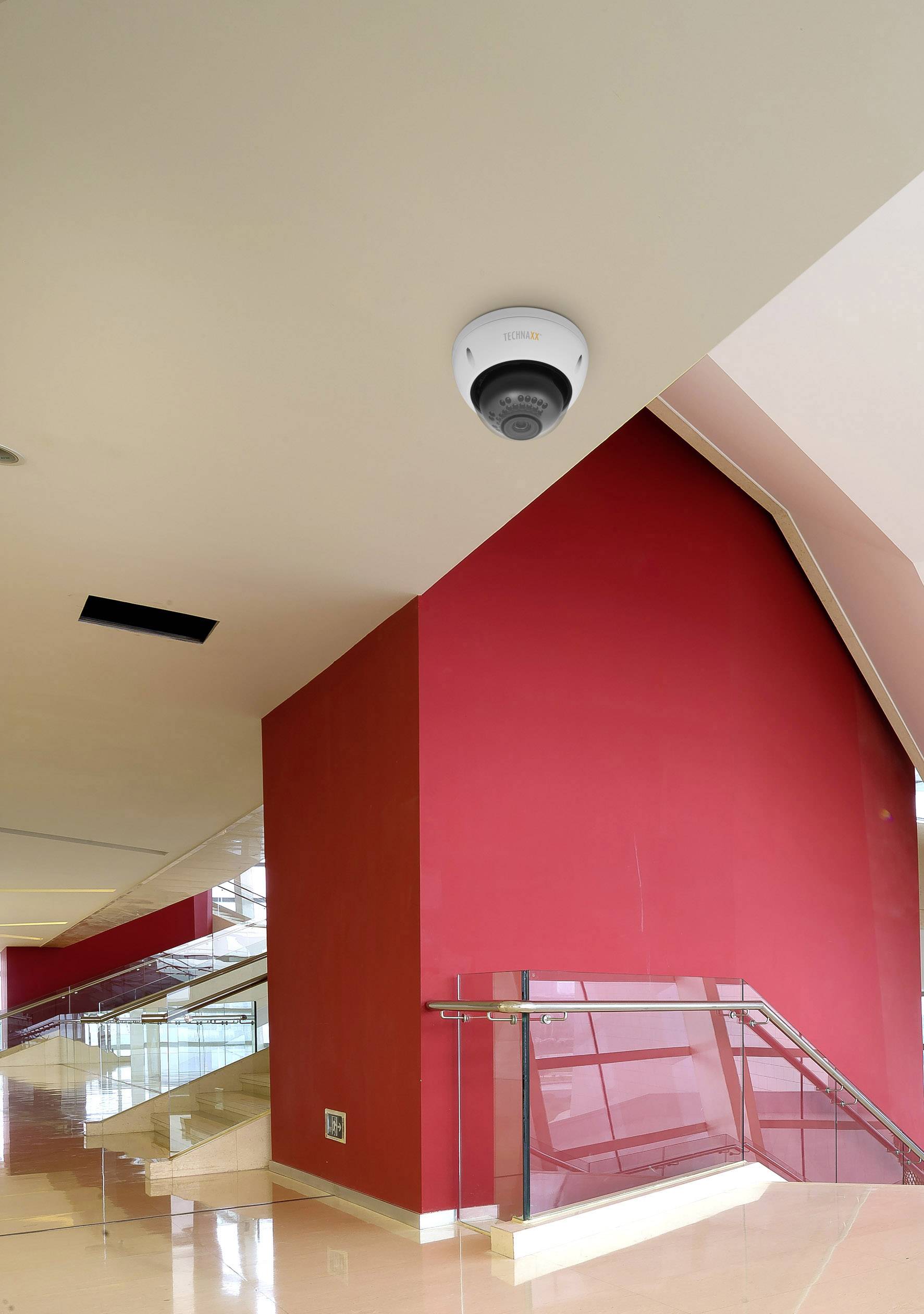Kamera monitorująca jest zamontowana na suficie nowoczesnego budynku z czerwonymi ścianami i szklaną balustradą.