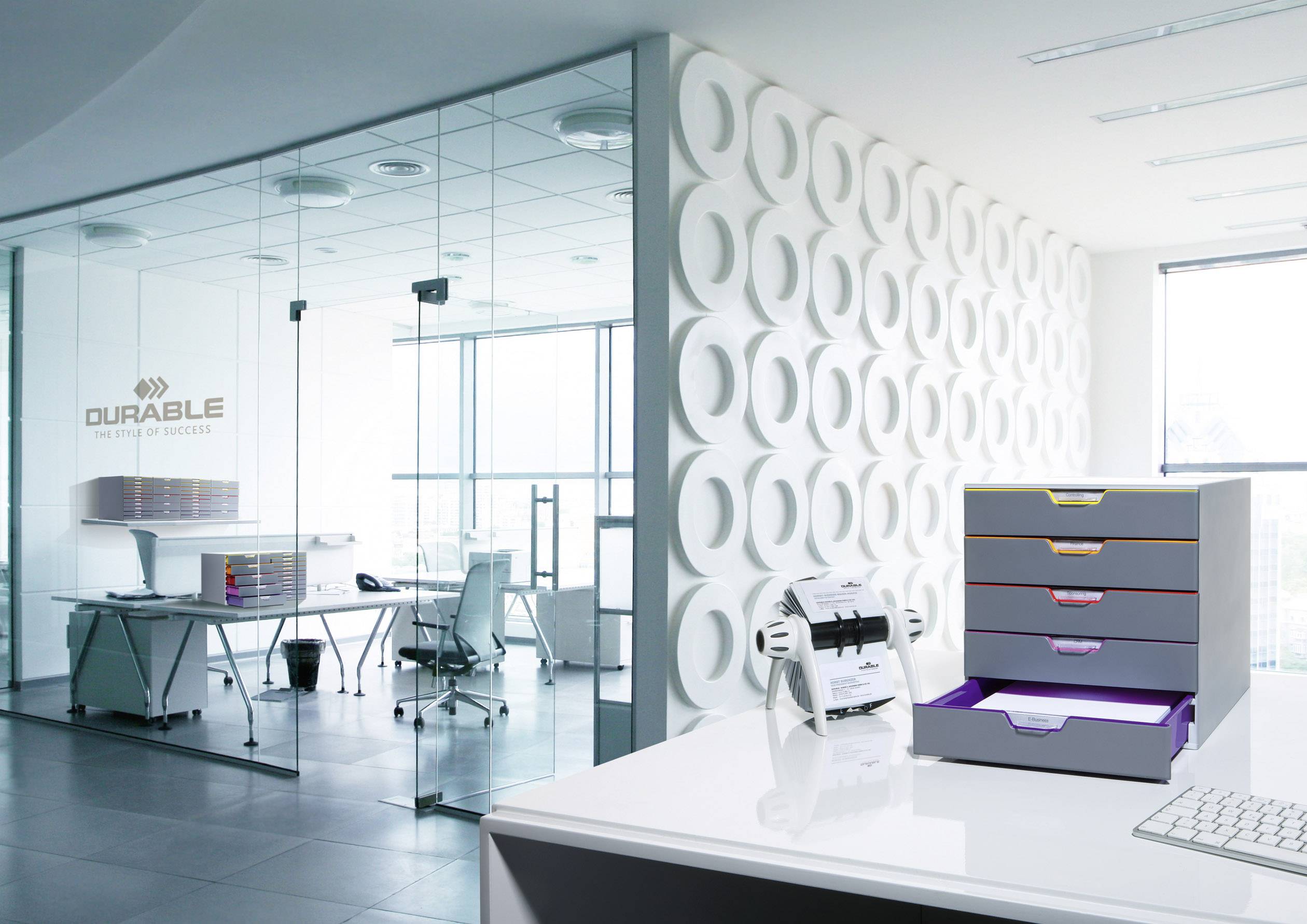 Nowoczesne biuro ze szklanymi ścianami i ergonomicznymi krzesłami. Na stole stoją pojemniki na dokumenty i segregator.