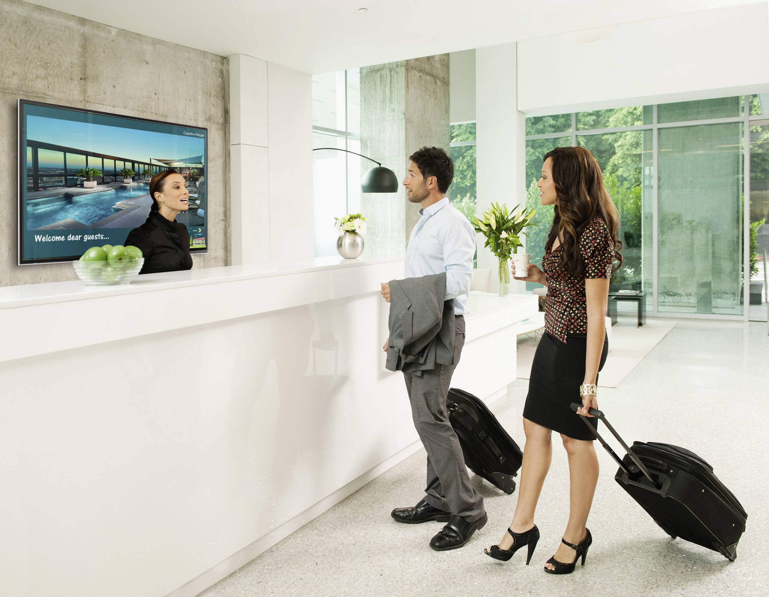 Mężczyzna i kobieta z torbami podróżnymi stoją przy recepcji i rozmawiają z recepcjonistką w nowoczesnym hotelu.