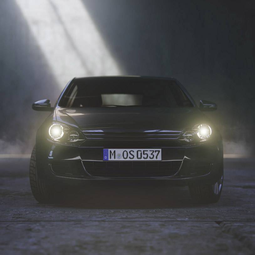 Czarne auto z włączonymi reflektorami stoi w ciemnym pomieszczeniu, oświetlone smugą światła padającą z góry.
