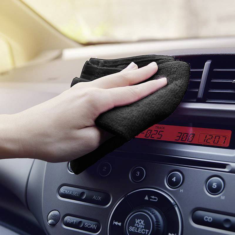 Ręka wyciera deską rozdzielczą samochodu szmatką, podczas gdy wyświetlacz samochodu pokazuje godzinę.