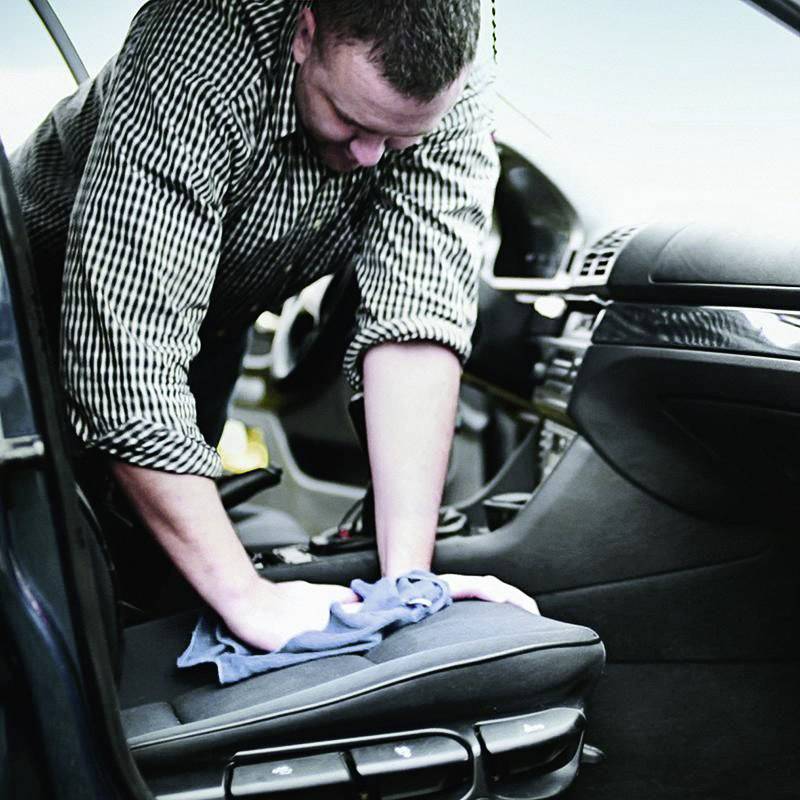 Osoba czyści siedzenie kierowcy samochodu niebieską szmatką. Wnętrze jest nowoczesne i schludne, z naciskiem na czystość.