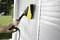 Osoba czyści białą roletę za pomocą myjki ciśnieniowej. W tle widać trawnik i drzewa.