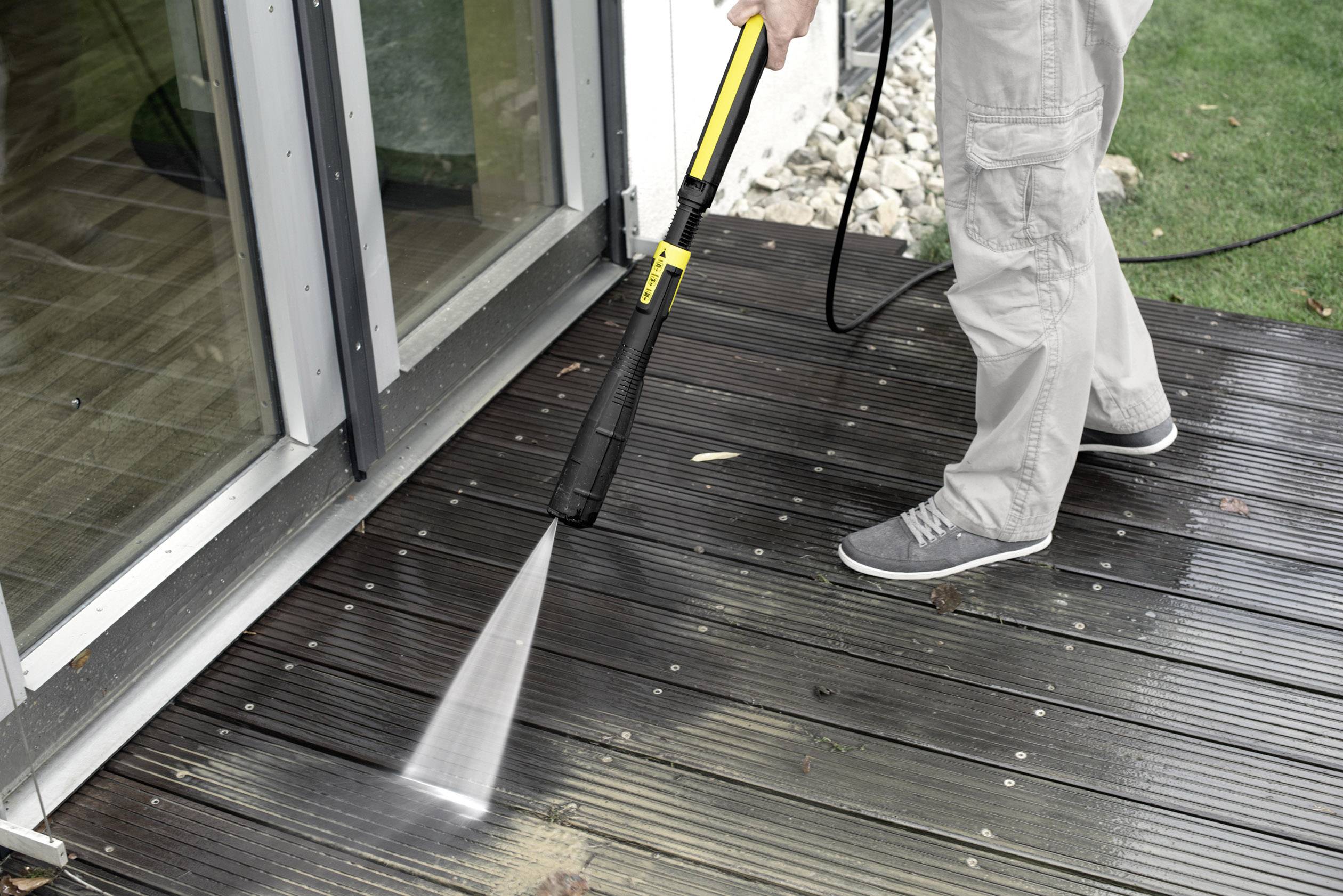Osoba czyści drewnianą tarasową za pomocą myjki ciśnieniowej obok przeszklonej bramy.