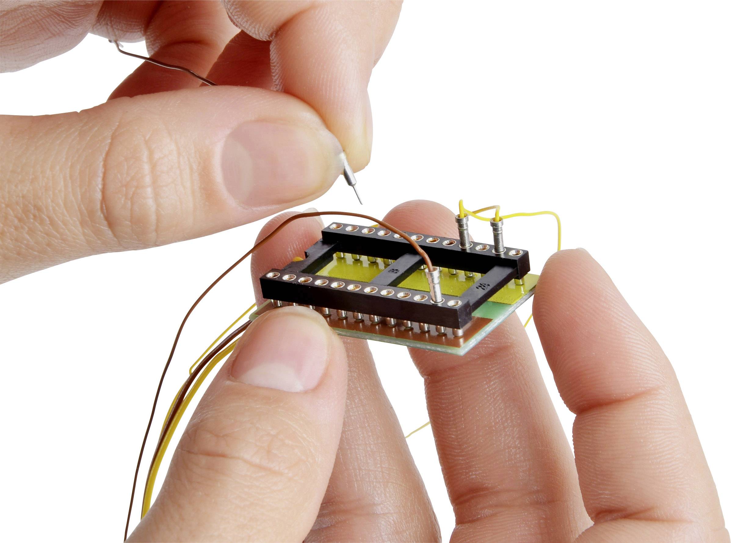 Osoba trzyma małą elektroniczną płytkę drukowaną i podłącza cienkie przewody do jej złączy.