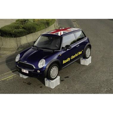 Niebieski Mini Cooper stoi na szarych plastikowych skrzynkach. Na boku samochodu widnieje napis 'Really Useful Box'. Dach ozdobiony jest flagą Wielkiej Brytanii.