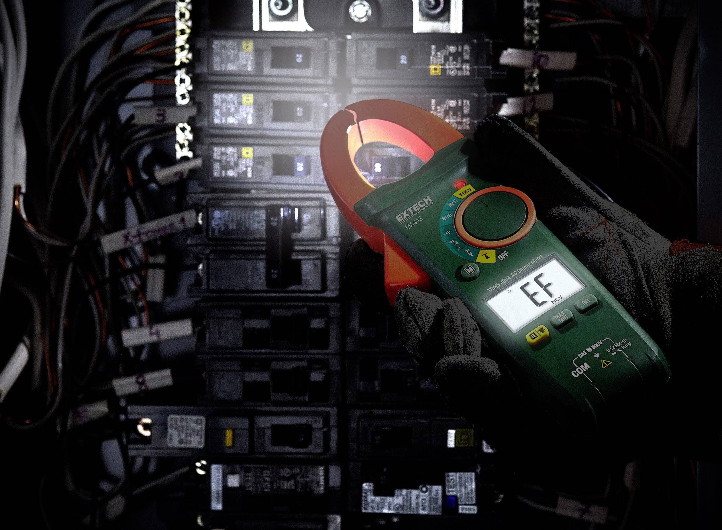 Elektryk mierzy natężenie prądu w skrzynce bezpiecznikowej za pomocą cęgów. Wyświetlacz pokazuje konkretną wartość.