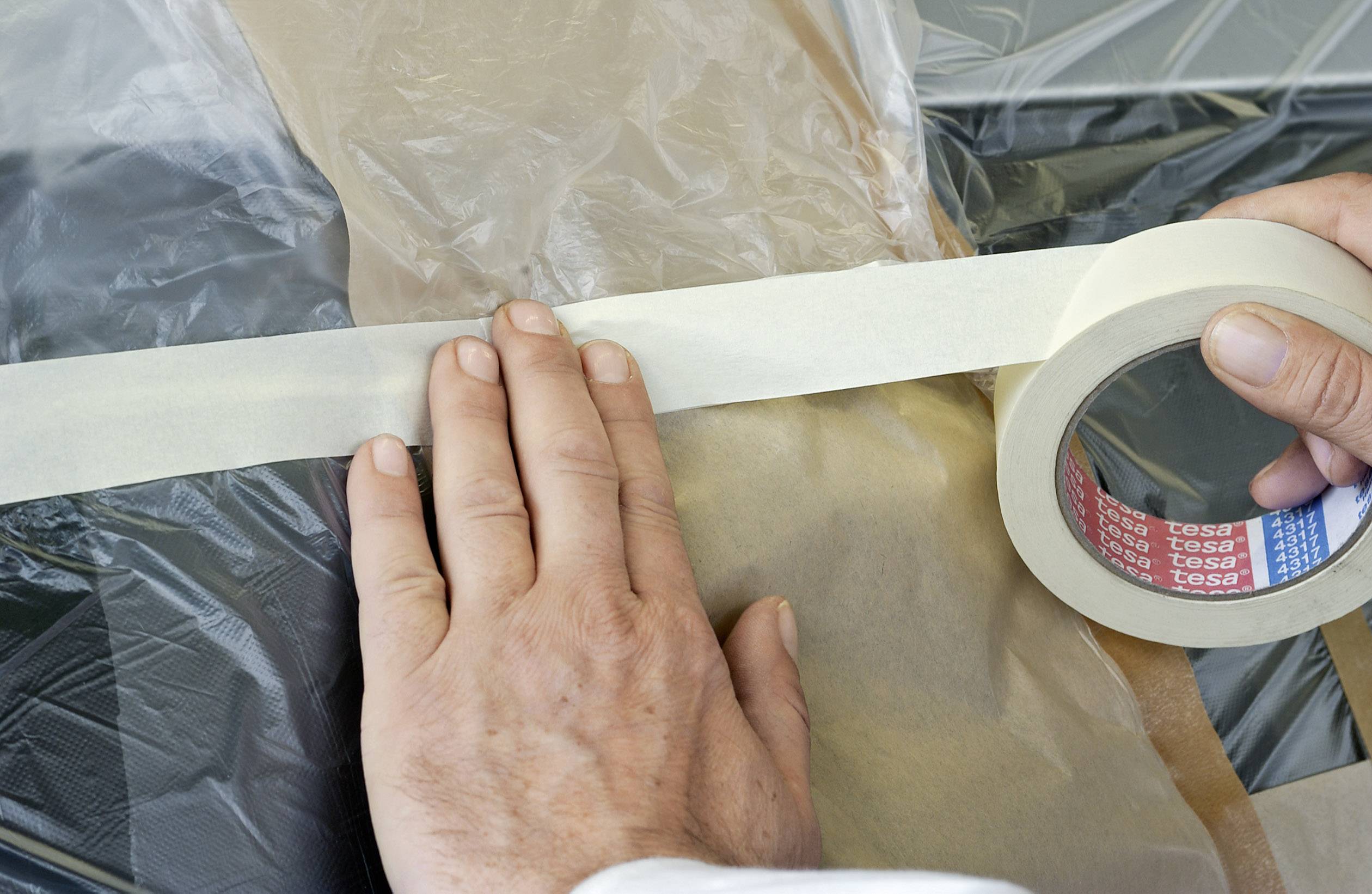 Osoba przykleja taśmę malarską do folii plastikowej, aby zabezpieczyć powierzchnie, najprawdopodobniej podczas malowania lub renowacji.