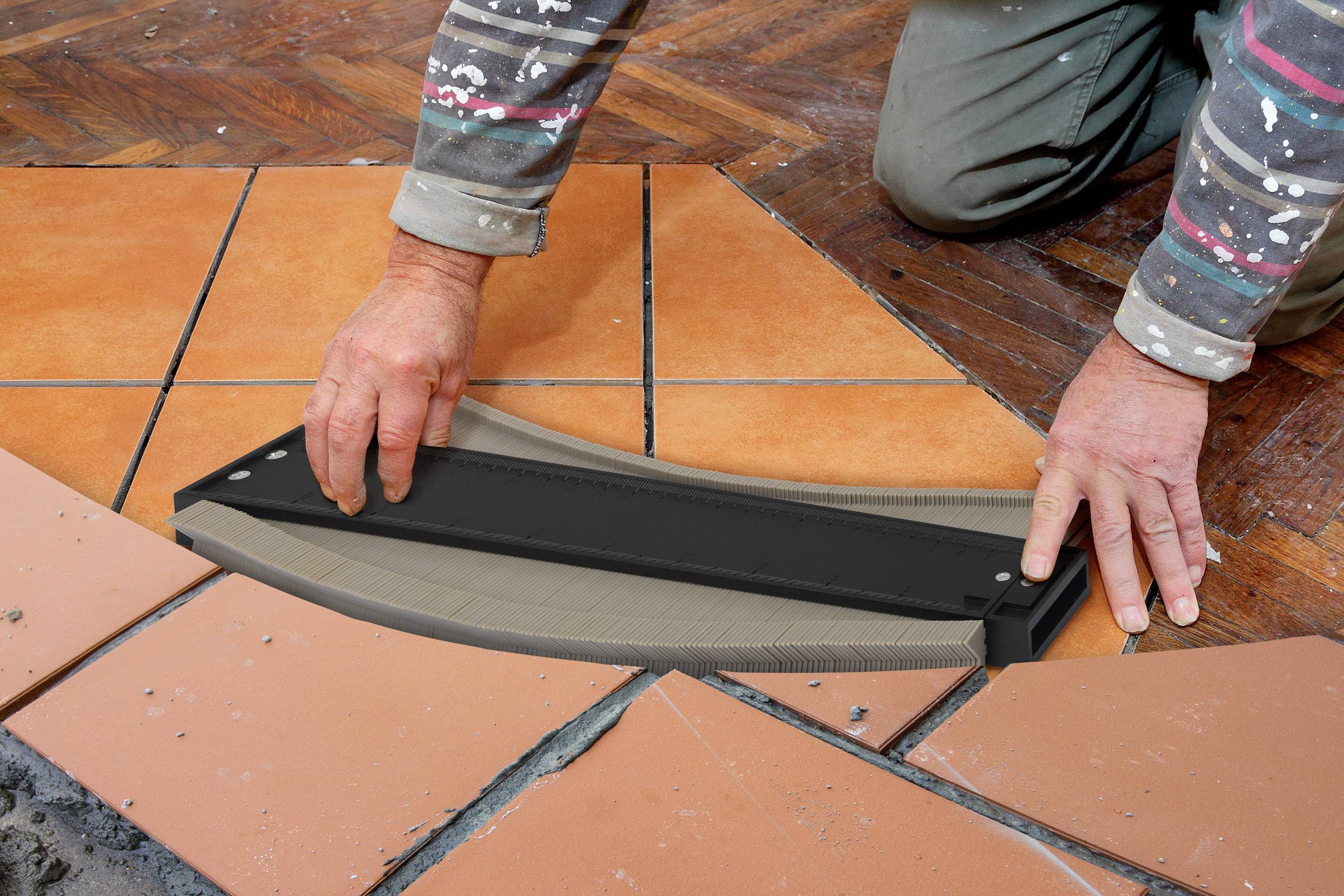 Pracownik rozmieszcza pomarańczowe płytki na podłodze, używając narzędzia do przycinania płytek przy krawędzi.