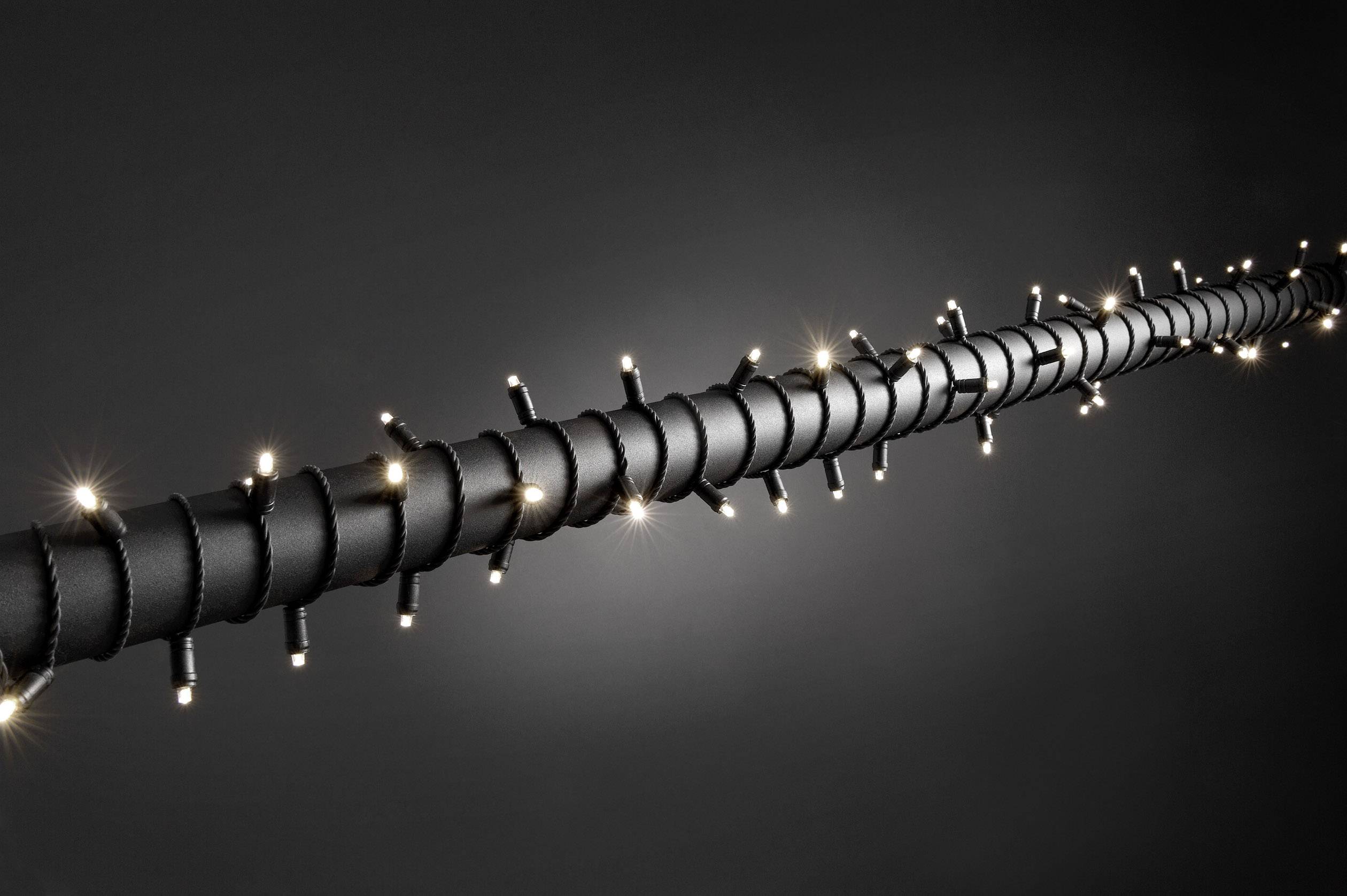 Czarny kabel, spiralnie owinięty małymi białymi światłami LED, świeci się na neutralno-szarym tle.