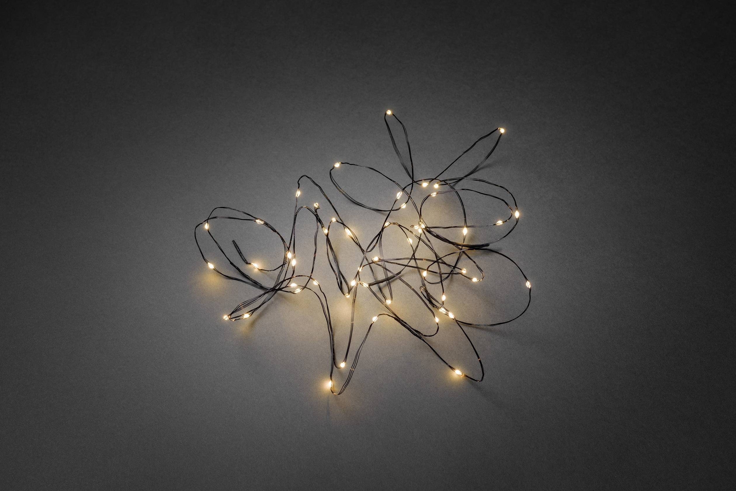 Nieporządnie ułożony łańcuch świetlny z małymi, ciepłobiałymi lampkami leży na szarym tle.