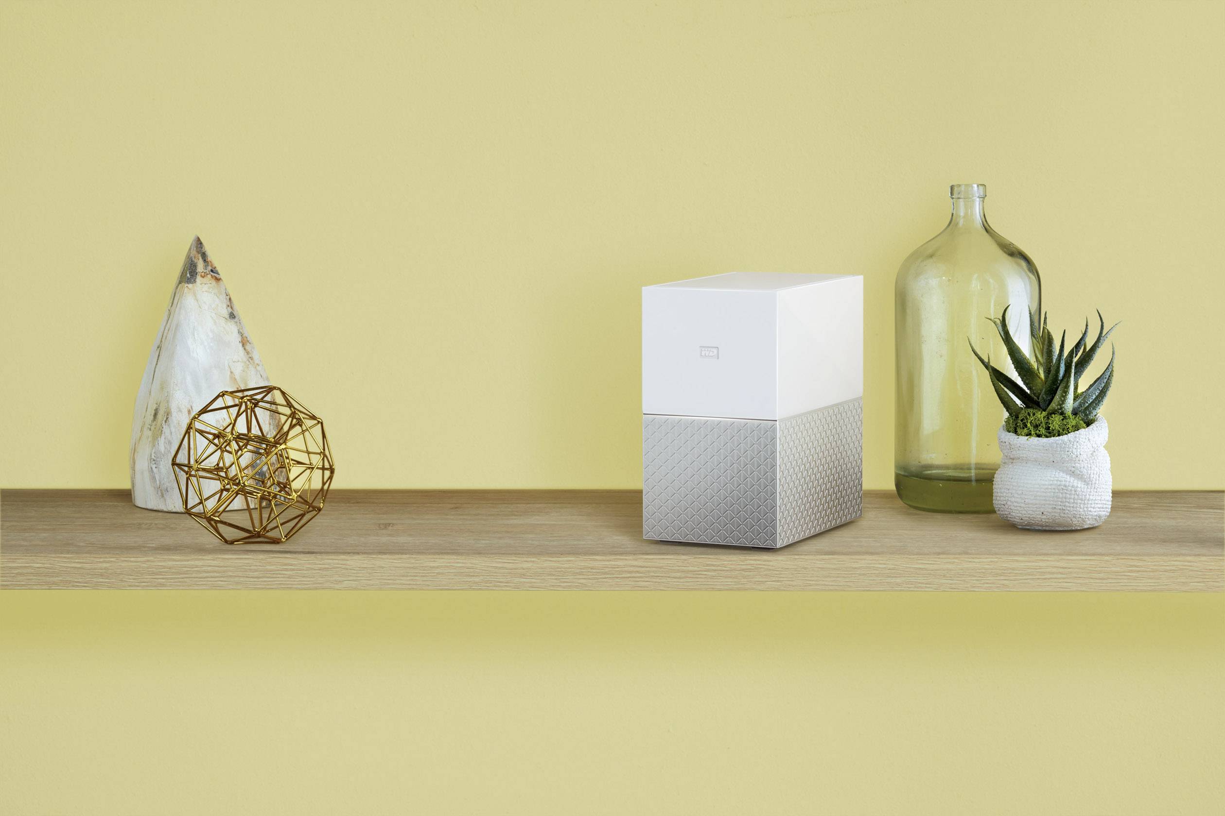 Minimalistycznie ozdobiona półka z geometryczną rzeźbą, nowoczesną kostką, dużą szklaną butelką i sukulentem.