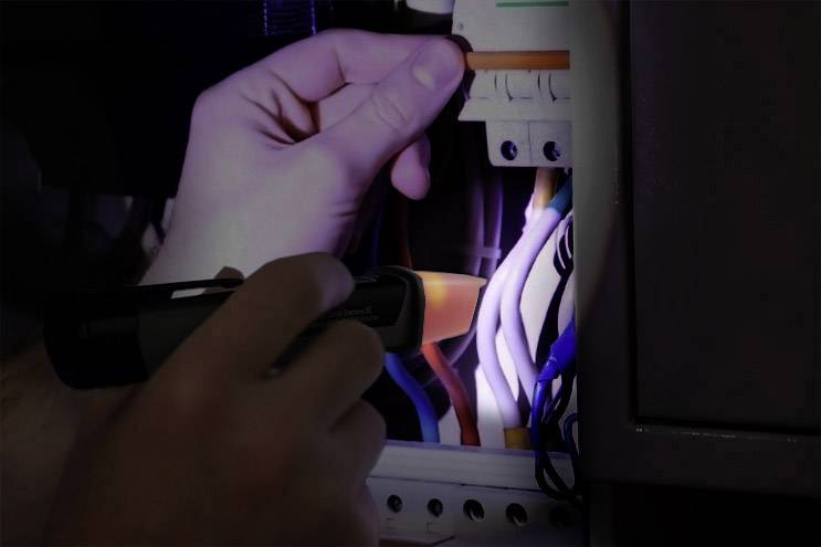 Osoba świeci latarką na kolorowe przewody w skrzynce bezpieczników.