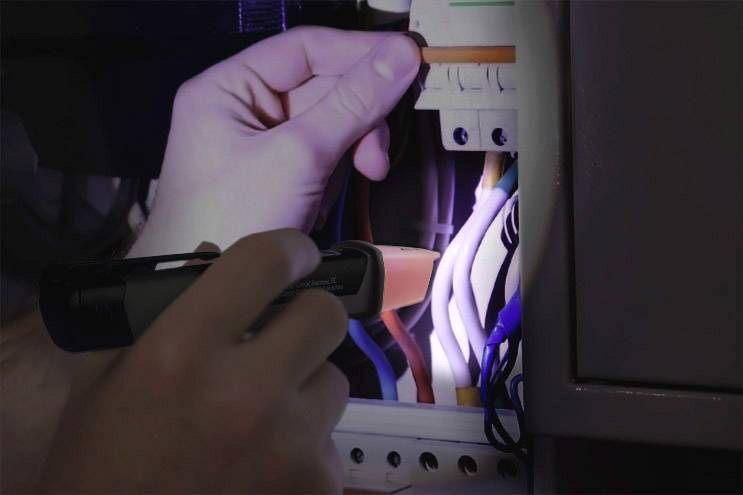 Osoba pracuje z latarką w otwartym obwodzie elektrycznym. Widoczne są różne przewody.