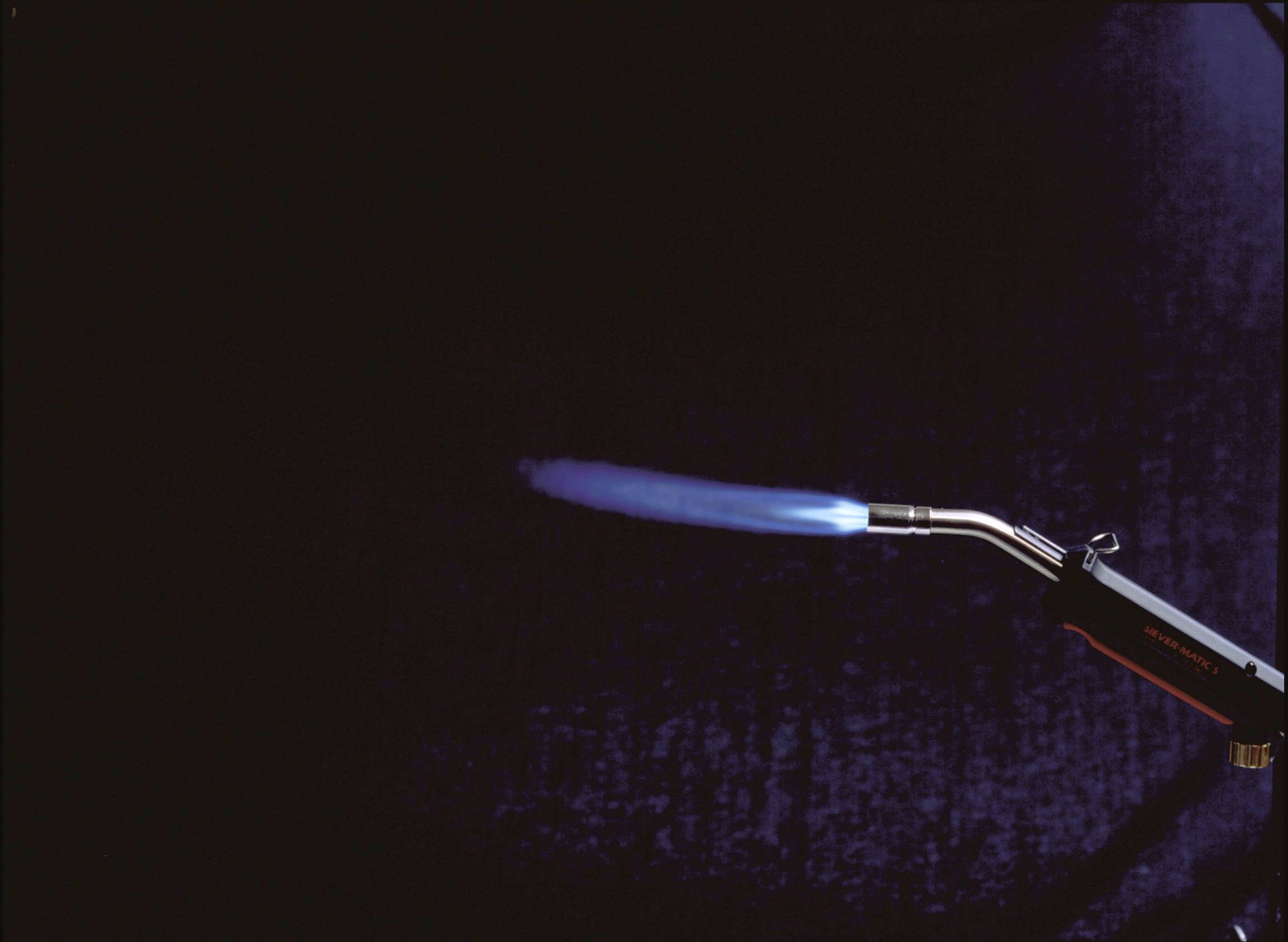 Lampa lutownicza z niebieskim płomieniem na ciemnym tle.