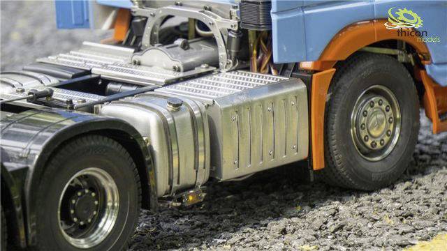 Modelowy samochód ciężarowy na żwirowej nawierzchni, z niebiesko-pomarańczowymi akcentami oraz widocznymi zbiornikami i silnikiem.