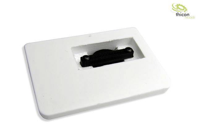 Biała prostokątna pokrywa z podłużnym wycięciem pośrodku, a wewnątrz czarny element. Logo 'Thicon models' w prawym górnym rogu.