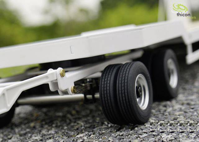 Zbliżenie przyczepy modelu pojazdu z czarnymi kołami na żwirowej nawierzchni, tło lekko rozmyte.