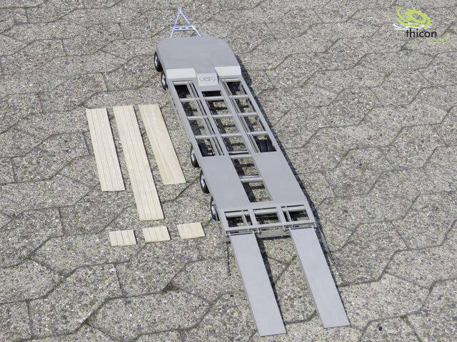 Model pustej przyczepy do transportu sześciu dużych kontenerów, obok której leżą deski drewniane, na utwardzonej nawierzchni.