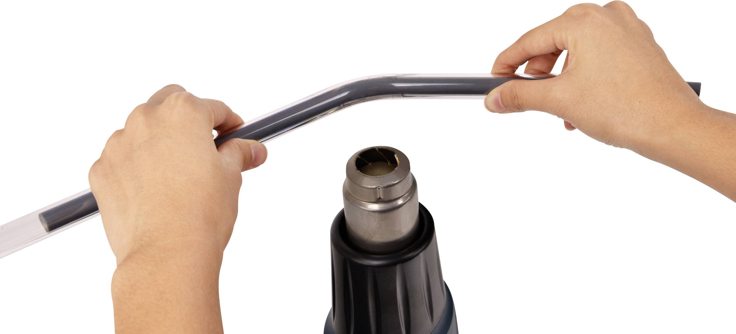 Dwie ręce trzymają rurę z tworzywa sztucznego nad dmuchawą gorącego powietrza, aby poprzez nagrzanie wygiąć rurę.