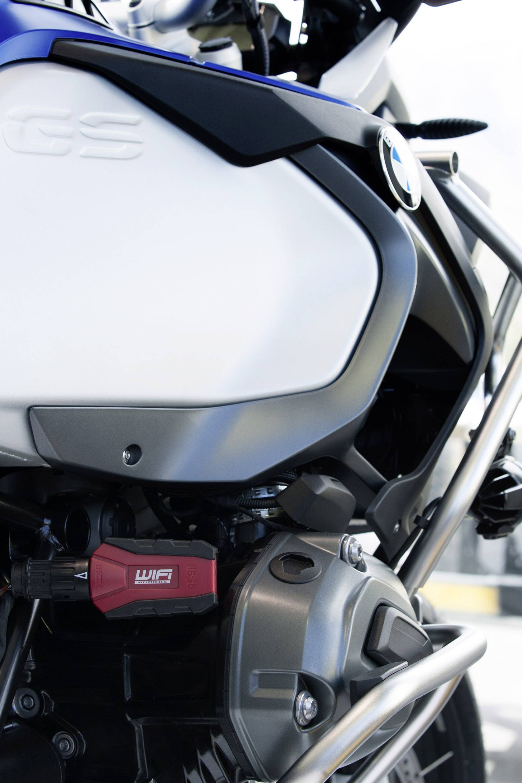 Szczegółowe zdjęcie motocykla przedstawia lewy obszar silnika jednośladu z niebiesko-białą owiewką i czerwonym elementem.