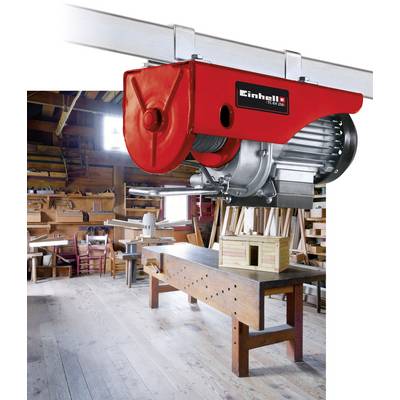 Czerwona wciągarka wisi na metalowym pręcie w warsztacie stolarskim. W tle widoczne są stoły warsztatowe, drewniane regały i narzędzia.