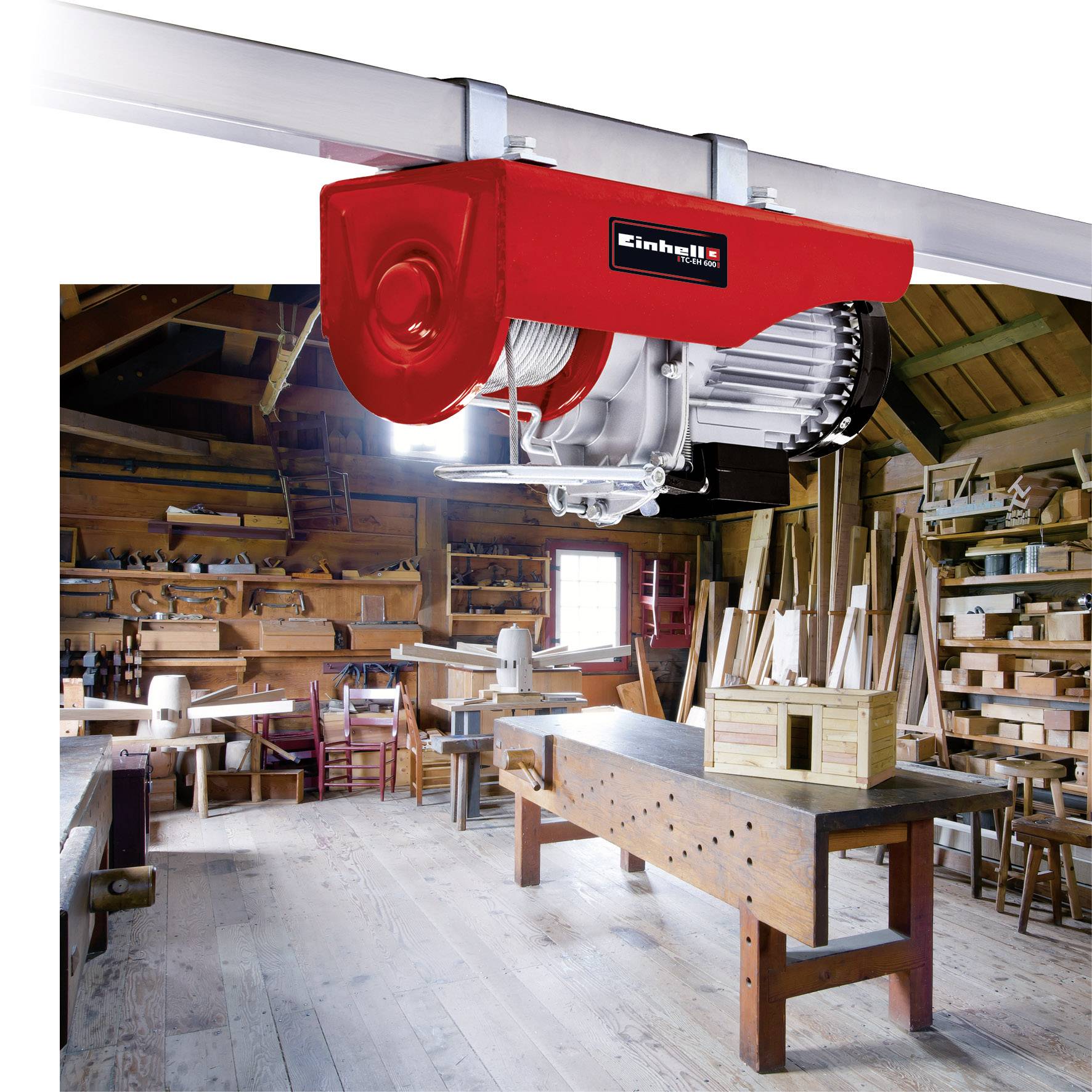 Warsztat stolarski z kilkoma stołami roboczymi i narzędziami. Na pierwszym planie zamontowany czerwony element maszyny sufitowej do obróbki drewna.