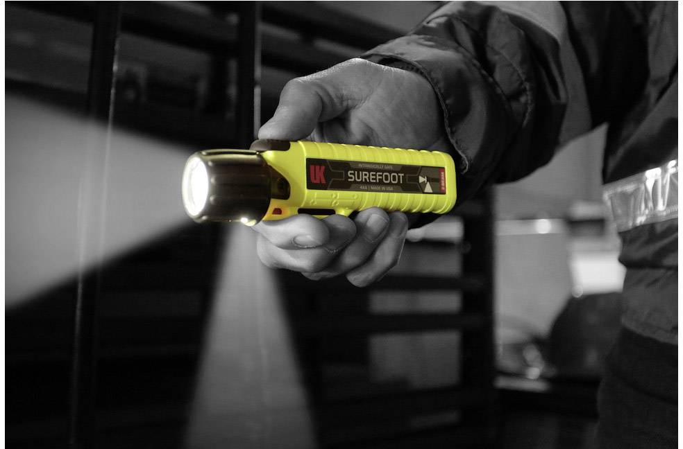 Osoba trzyma żółtą latarkę, która świeci w ciemnym pomieszczeniu. Fokus jest skupiony na dłoni i latarce.