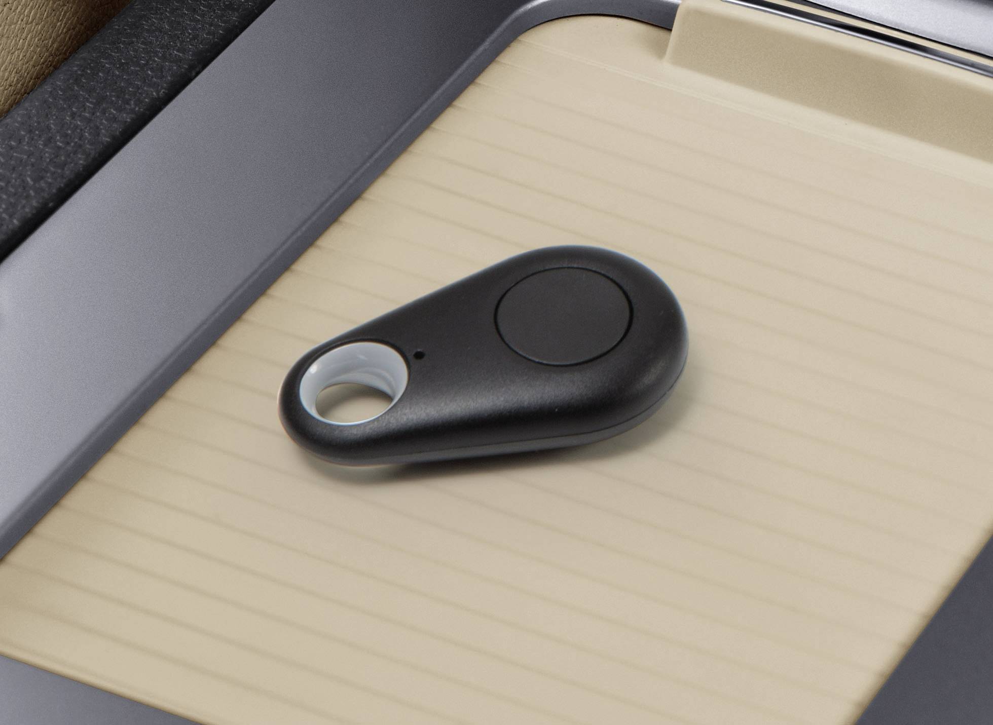 Czarny lokalizator kluczy z przyciskiem i otworem na brelok leży na beżowo-prążkowanym podłożu.