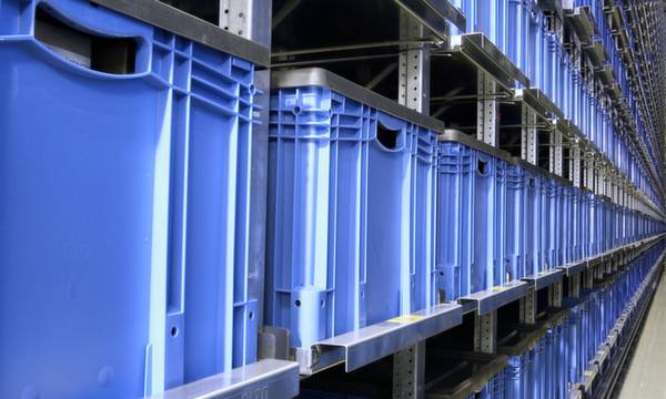 Niebieskie pojemniki plastikowe na regale magazynowym, ułożone w długich rzędach, obrazują zorganizowaną gospodarkę magazynową w środowisku przemysłowym.