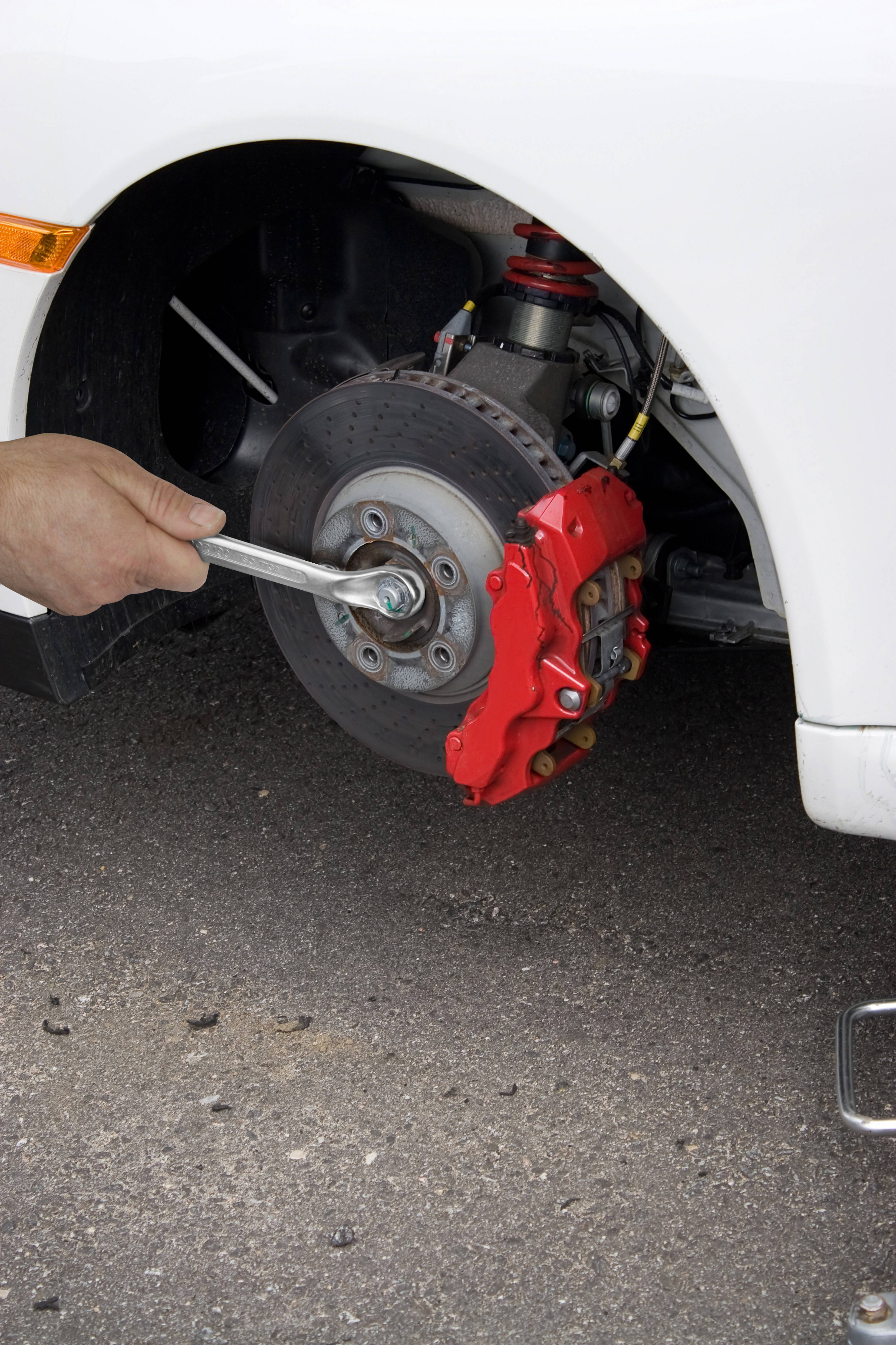 Jedna osoba dokręca śrubę na piaście koła przy pomocy klucza, podczas gdy pracuje przy hamulcu samochodu.